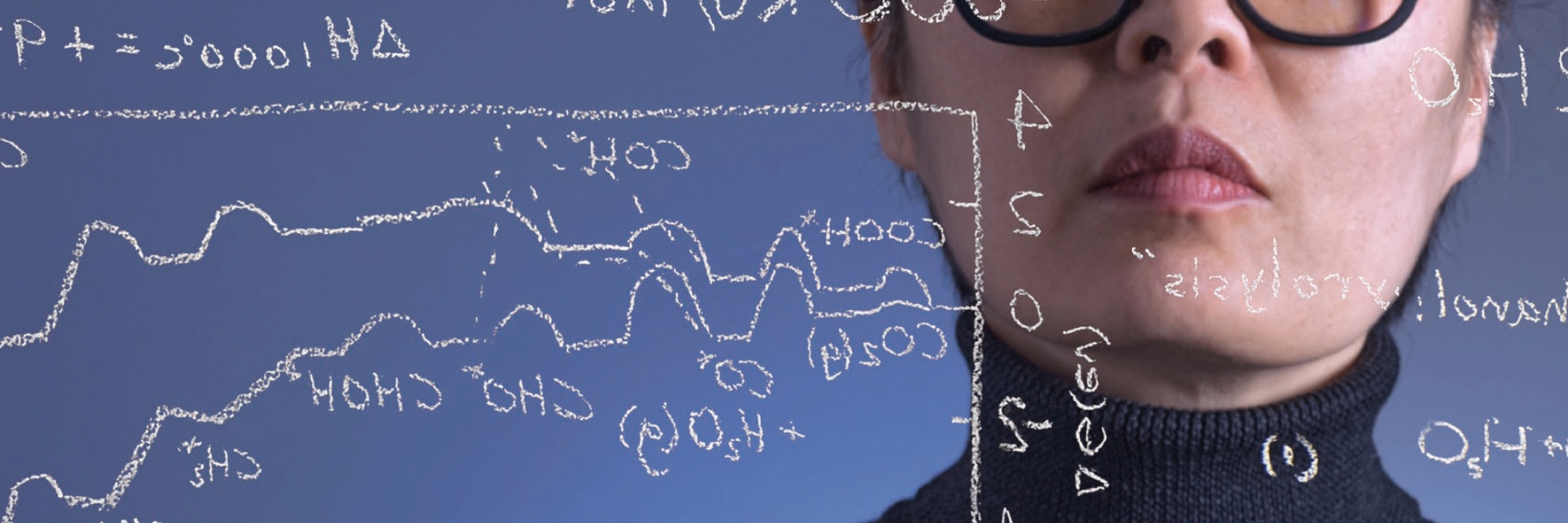 A woman writing symbols and equations on a glass board with white chalk.