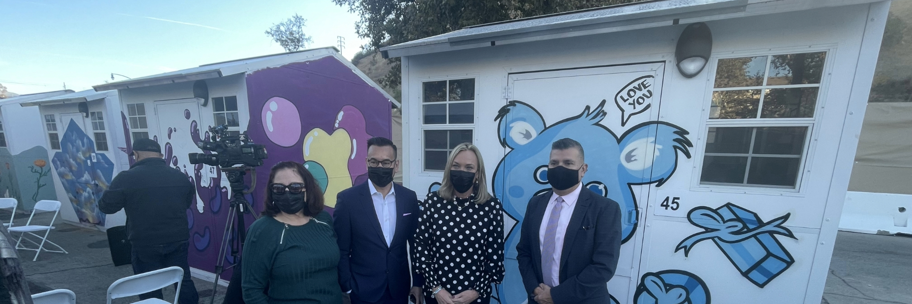 People posing for image in front of tiny homes at a press event