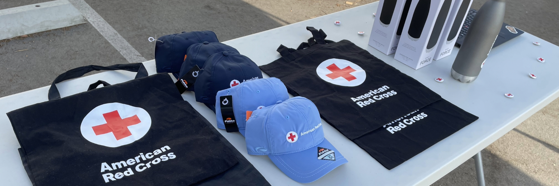 A table with american red cross hates, bags, and tumblers on it.