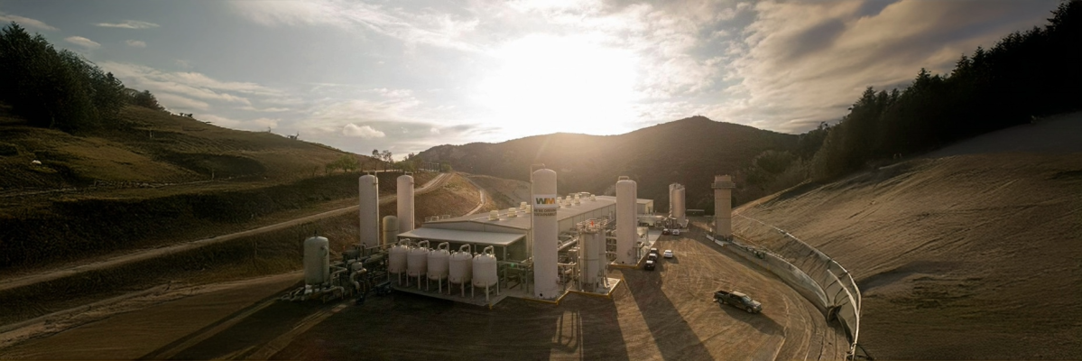 Waste management facility up against a hill with the sun starting to shine behind the hill